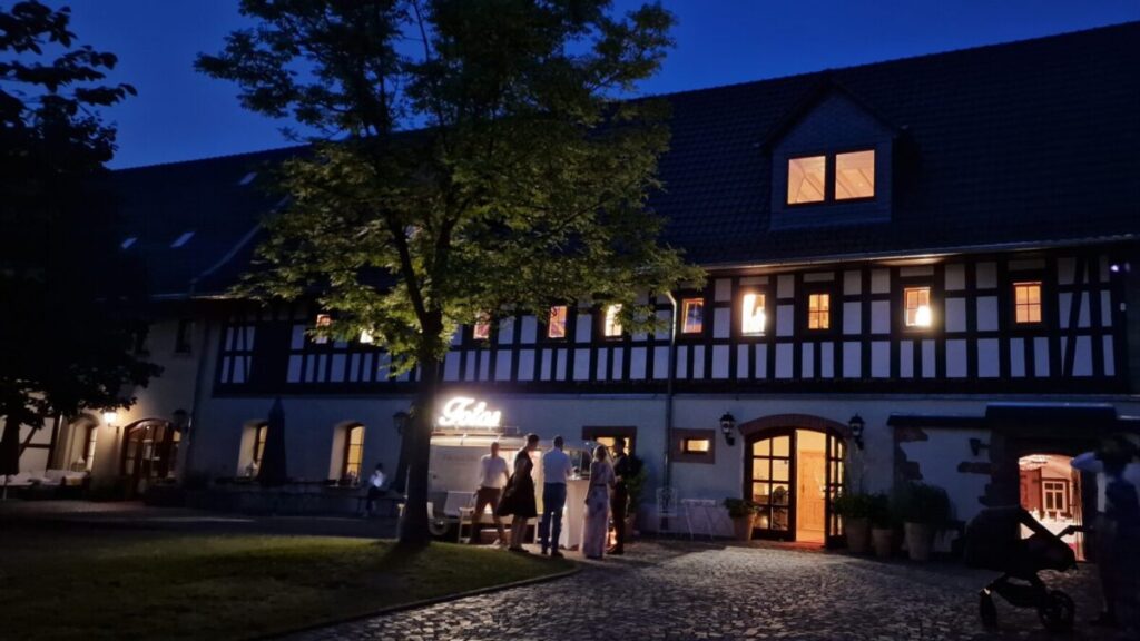 Stimmungsvoll beleuchteter Gutshof bei Nacht mit Gästen vor dem Eingangsbereich – Landpension Am Silberberg in Oberwiera